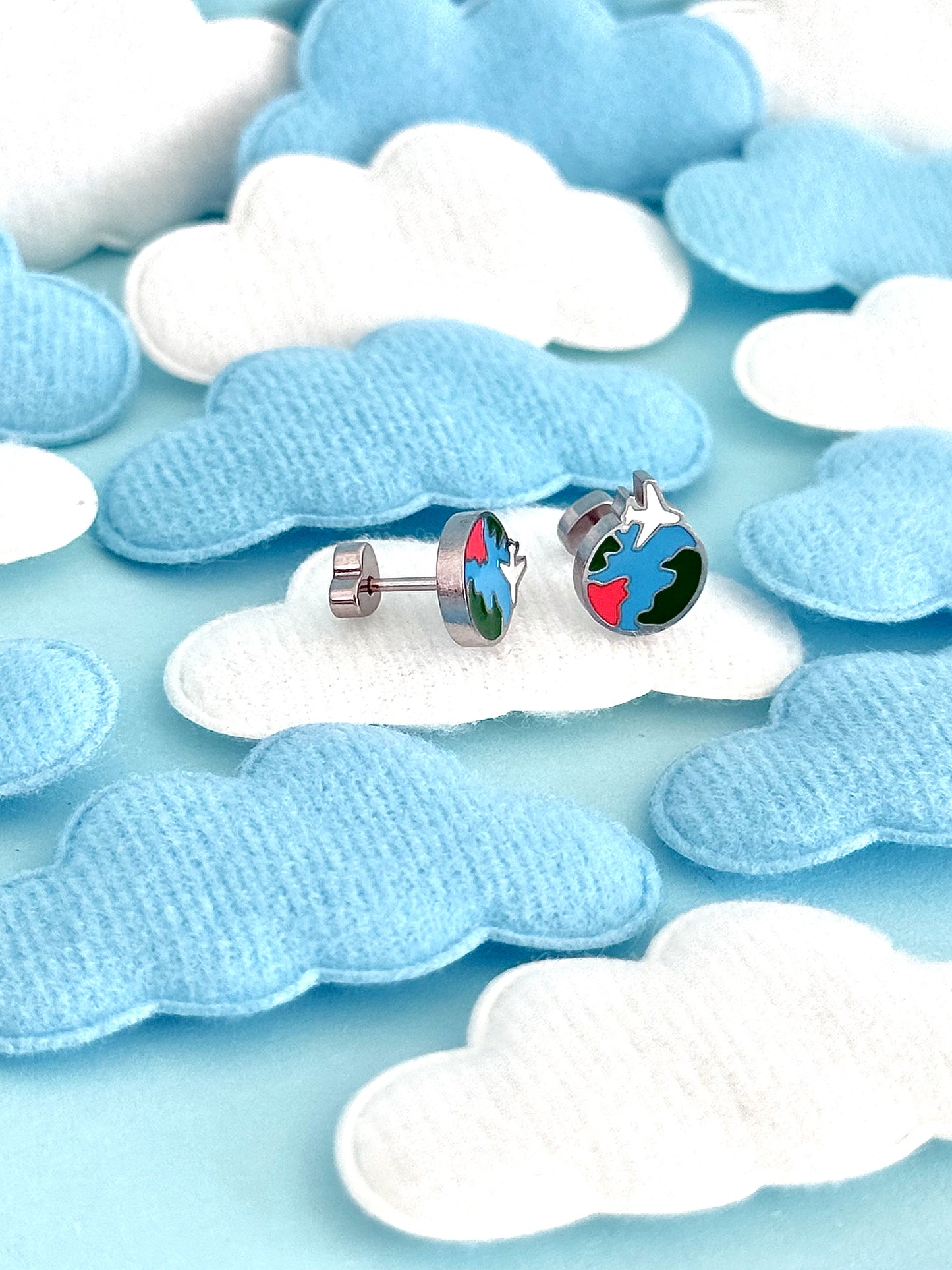 A pair of kids small hypoallergenic round silver screwback stud earrings with colorful enamel details, displayed on a white cloud-shaped stand against soft cloud cutouts from The pierced peanut earring co.