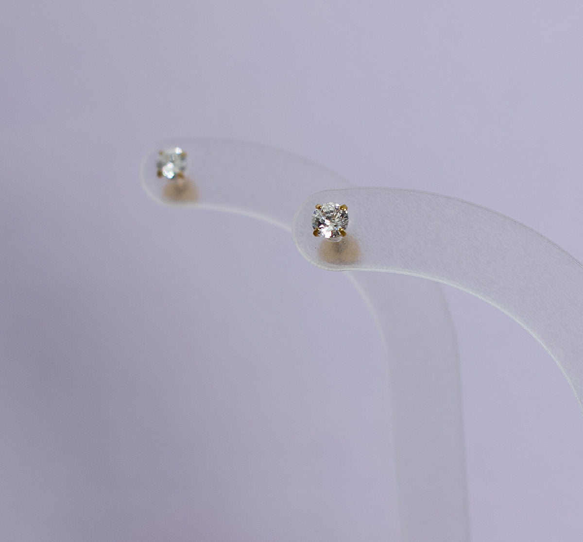 A clear acryllic stand holding a pair of kida hypoallergenic gold diamond stud earrings with heart shaped screwbacks. Earrings are from the Pierced Peanut in Nz