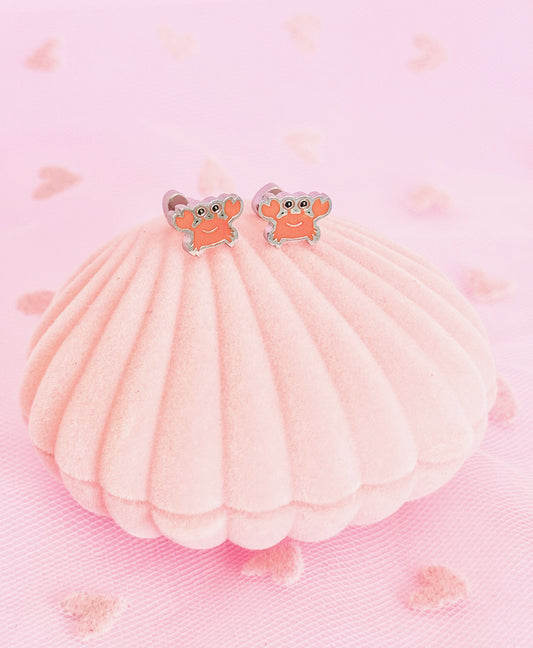 A pair of silver hypoallergenic kids crab shaped screwback stud earrings from The Pierced Peanut Earring Co displayed on a pink clam shell box.