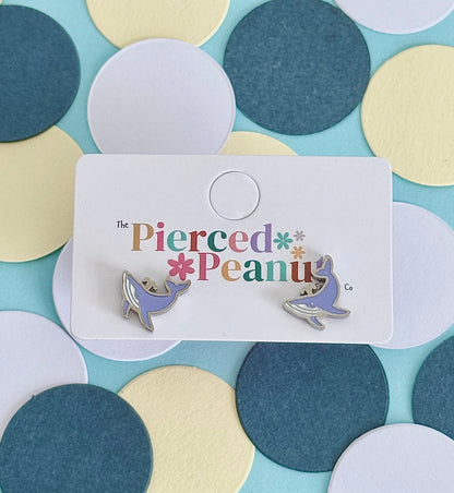 A pair of kids hypoallergenic, silver, whale-shaped screwback stud earrings with enamel blue details on a jewellery card from The Pierced Peanut Earring Co.