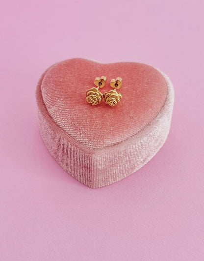 Kids hypoallergenic gold rose-shaped screwback stud earrings on a pink heart-shaped jewelry box against a pink background. Earrings are from the Pierced Peanut in NZ.
