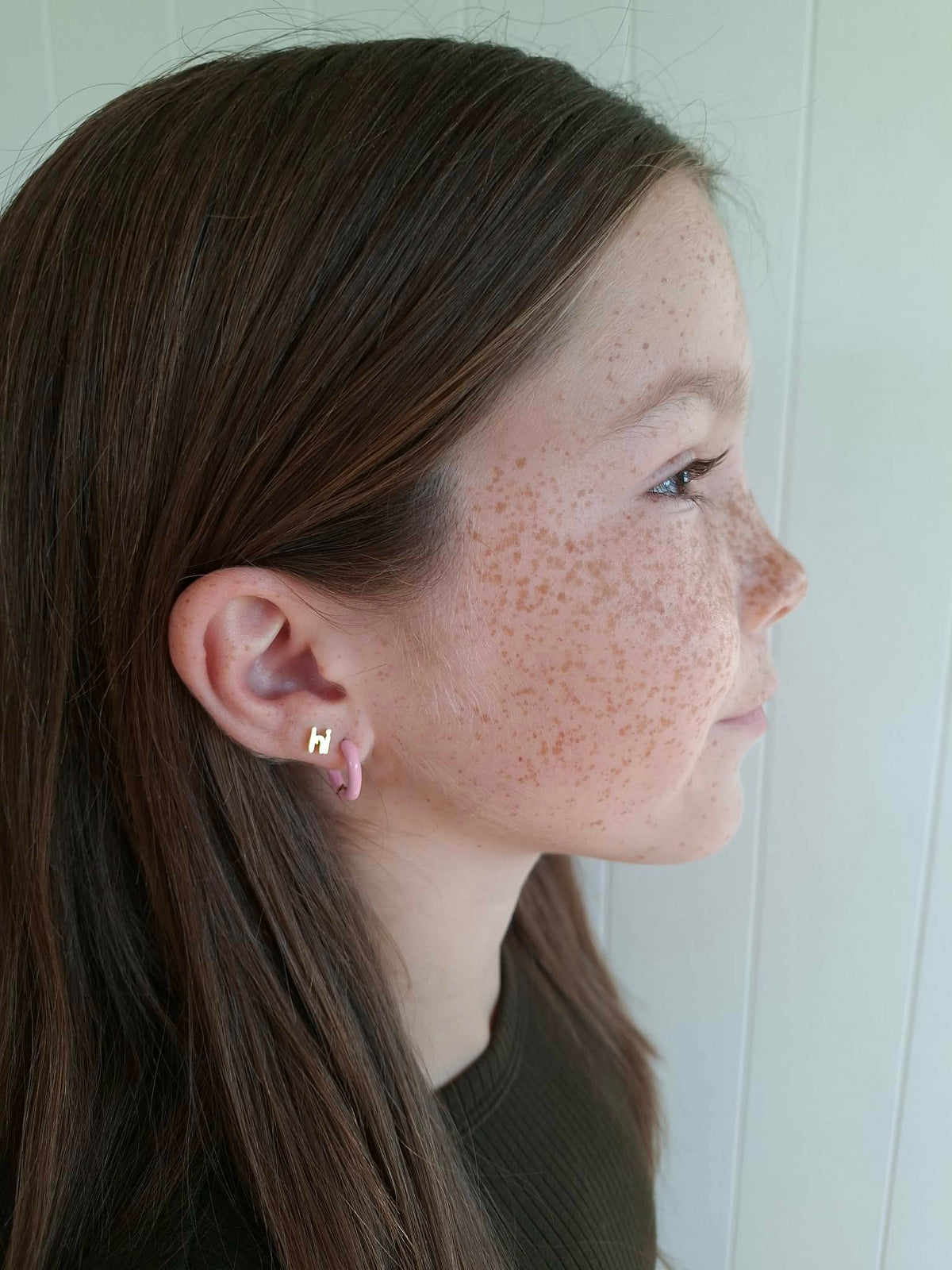 Side view of a girl wearing pastel pink hypoallergenic huggie hoop earrings and a gold screwback stud earring saying "hi" from the Pierced Peanut.