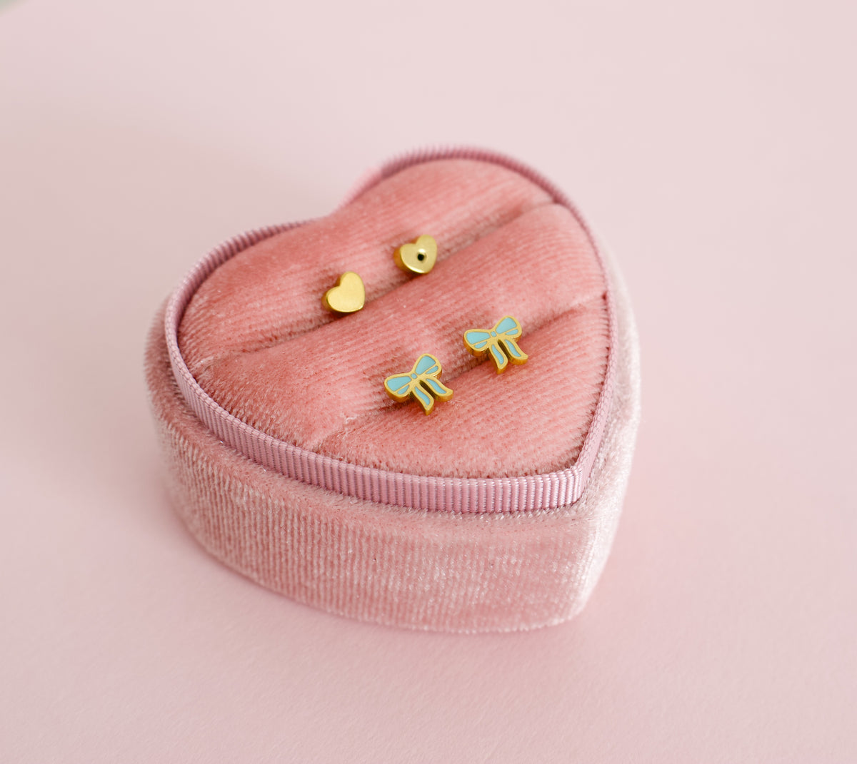 hypoallergenic blue bow shaped screwback kids earrings displayed in a pink heart box