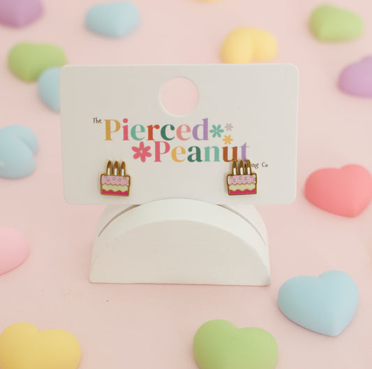 A pair of small hypoallergenic cake-shaped screwback stud earrings displayed on a white branded card from the Pierced Peanut earring co