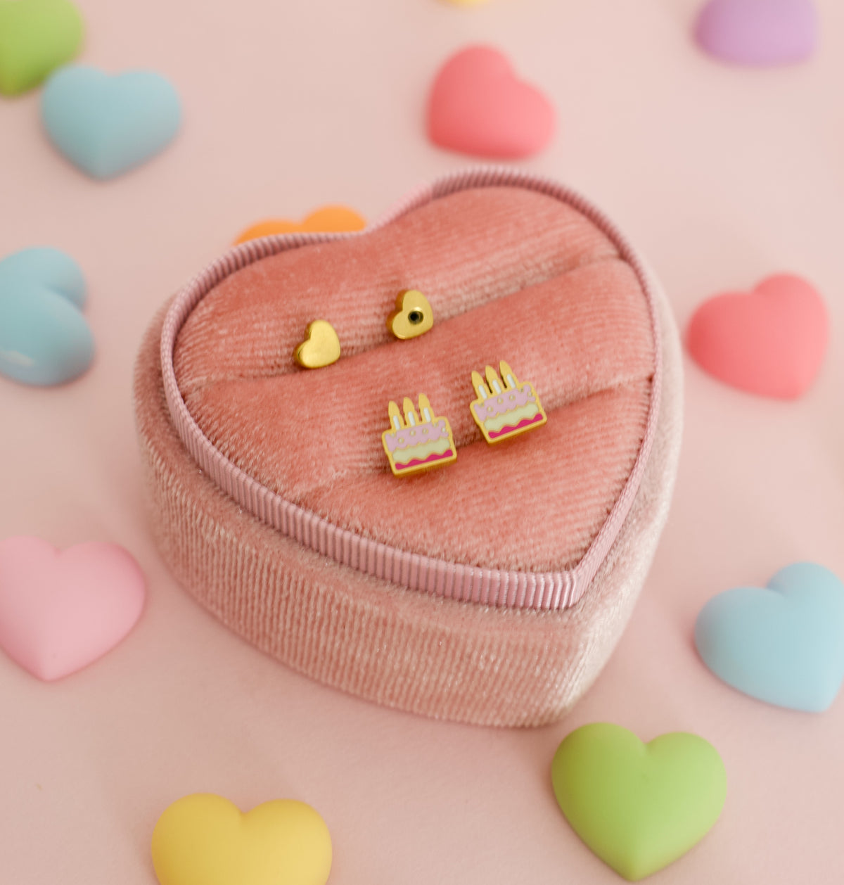 A pair of small hypoallergenic cake-shaped screwback stud earrings displayed on a white branded card from the Pierced Peanut earring co