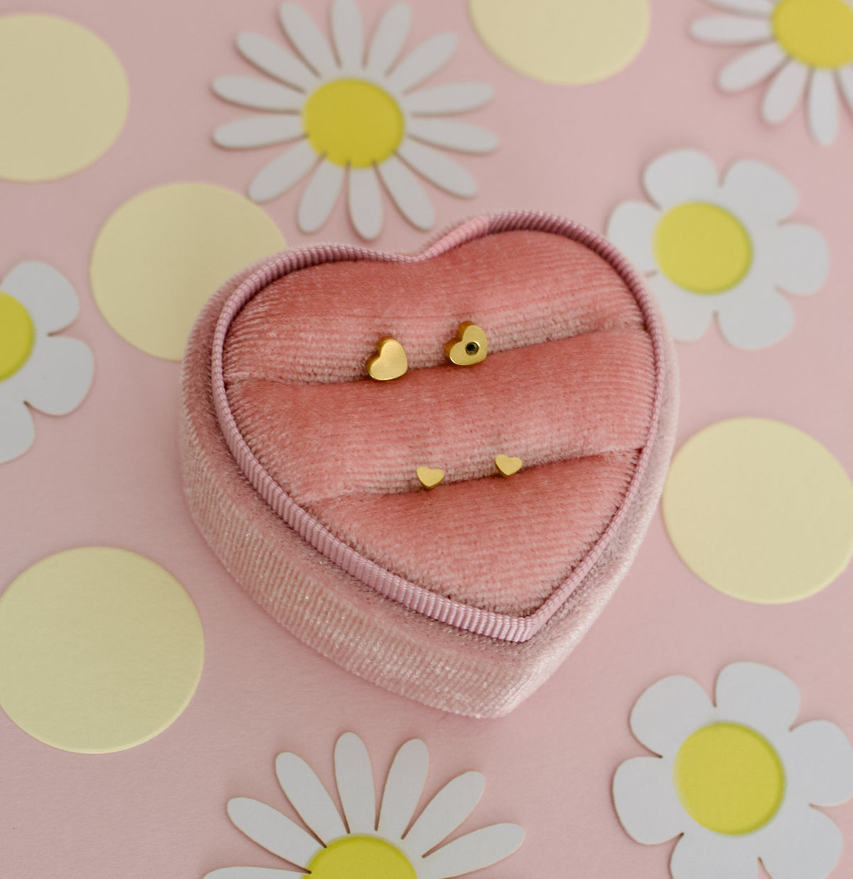 A pair of small hypoallergenic dainty heart screwback stud earrings displayed on a pink jewellery box display from the Pierced Peanut earring co.
