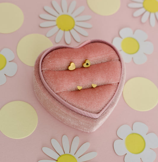 A pair of small hypoallergenic dainty heart screwback stud earrings displayed on a pink jewellery box display from the Pierced Peanut earring co.