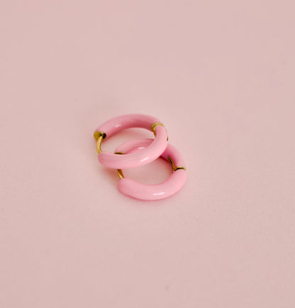 Two small hypoallergenic pink hoop earrings with gold-tone metal tips, arranged overlapping on a soft pink background from the Pierced Peanut.
