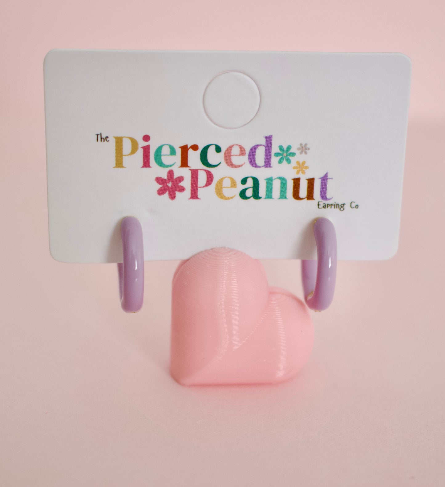 A pair of hypoallergenic hoop huggie earrings displayed on a white backing card with the brand name 'The Pierced Peanut Earring Co' printed in colorful text. 
