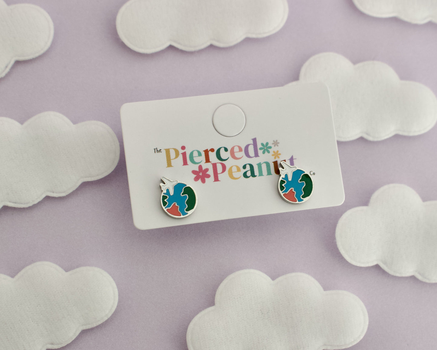 A pair of kids small hypoallergenic round silver screwback stud earrings with colorful enamel details, displayed on a white cloud-shaped stand against soft cloud cutouts from The pierced peanut earring co.