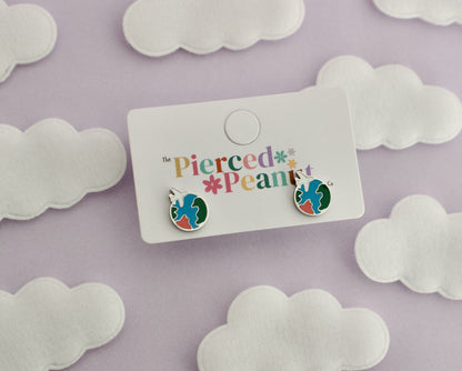A pair of kids small hypoallergenic round silver screwback stud earrings with colorful enamel details, displayed on a white cloud-shaped stand against soft cloud cutouts from The pierced peanut earring co.