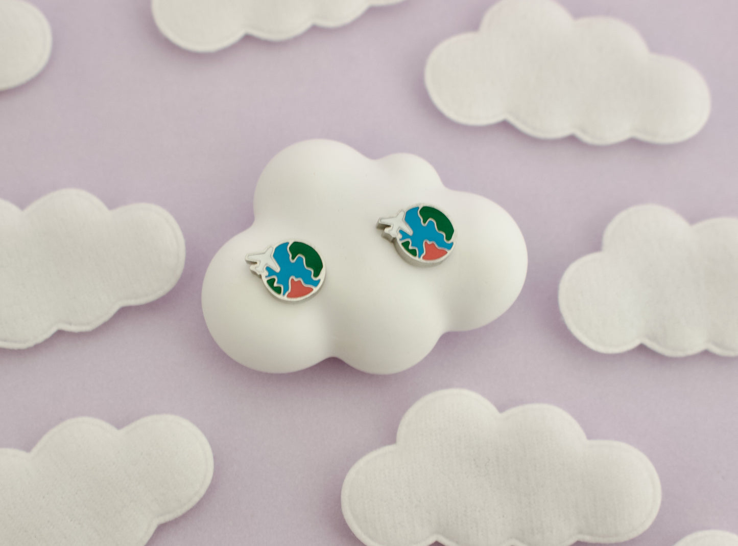 A pair of kids small hypoallergenic round silver screwback stud earrings with colorful enamel details, displayed on a white cloud-shaped stand against soft cloud cutouts from The pierced peanut earring co.