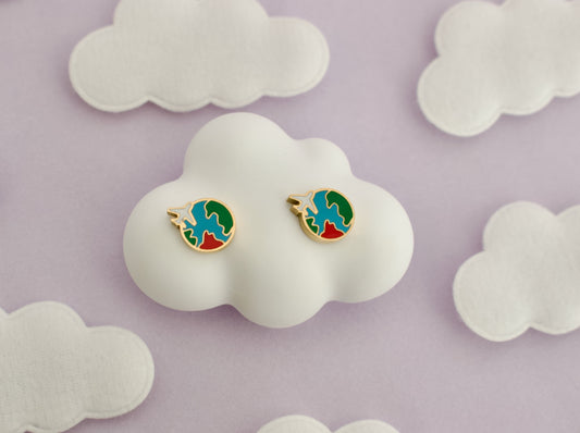 A pair of kids small hypoallergenic round gold-tone screwback stud earrings with colorful enamel details, displayed on a white cloud-shaped stand against a soft lavender background with white cloud cutouts.