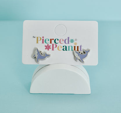 A pair of kids hypoallergenic, silver, whale-shaped screwback stud earrings with enamel blue details on a jewellery card from The Pierced Peanut Earring Co.