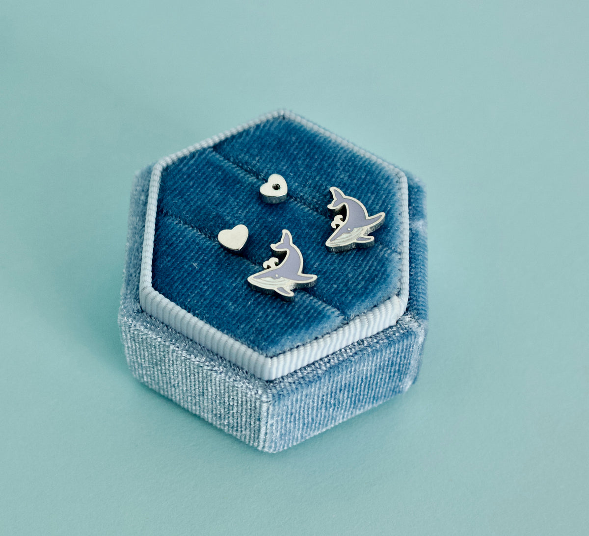 A pair of kids hypoallergenic, silver, whale-shaped screwback stud earrings with enamel blue details. Displayed on a blue jewellery box from The Pierced Peanut Earring Co.