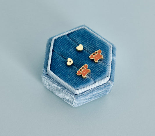 A pair of kids hypoallergenic, gold, crab screwback stud earrings with enamel orange details displayed in a blue jewellery box from The Pierced Peanut Earring Co.