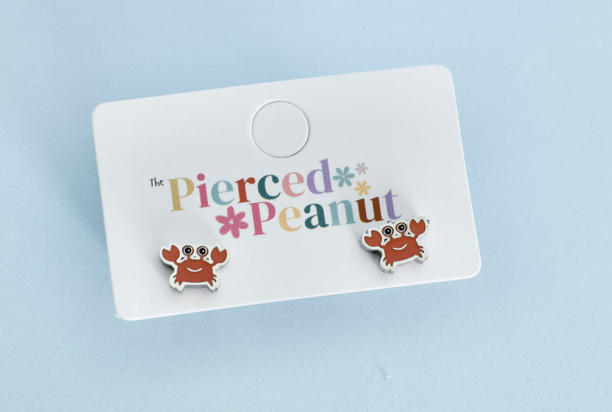 A pair of silver hypoallergenic kids crab shaped screwback stud earrings from The Pierced Peanut Earring Co displayed on a branded jewellery card in NZ.