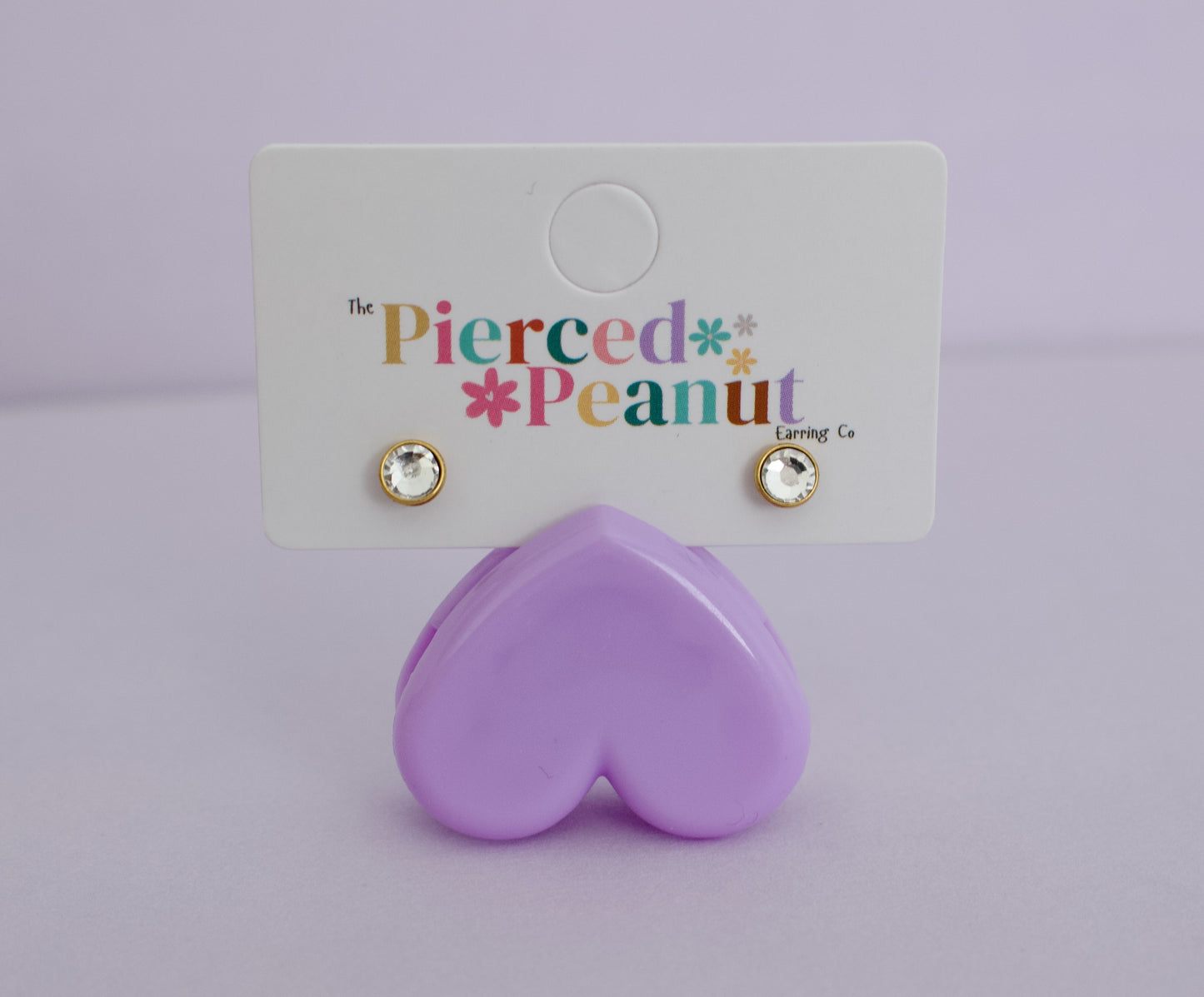 A pair of kids gold hypoallergenic round diamond stud bezel cut earrings. Displayed on a branded jewellery card reading The Pierced Peanut Earring Co, based in New Zealand.