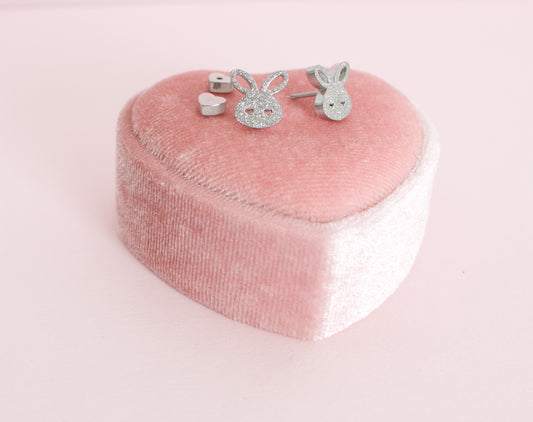 A pair of kids hypoallergenic textured sparkly silver bunny screwback stud earrings, displayed on a small pink velvet heart-shaped jewellery box against a soft pink background. The earrings are from The Pierced Peanut Earring Co based in New Zealand.