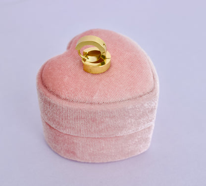 A pair of kids hypoallergenic gold hoop huggie earrings displayed on a pink heart box from The Pierced Peanut Earring Co in New Zealand, NZ.
