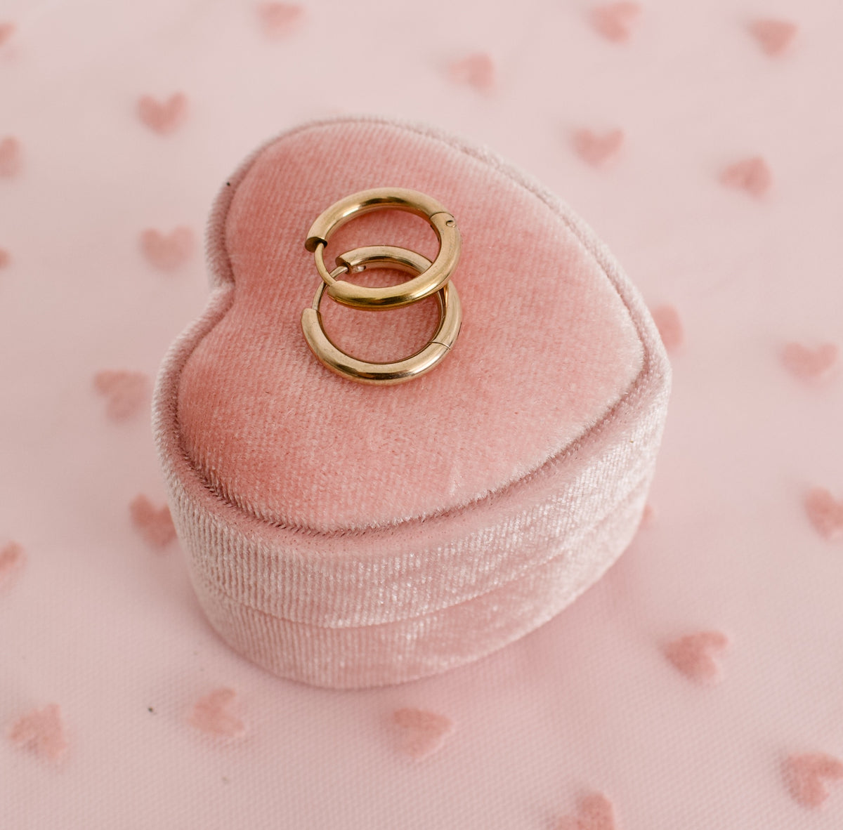 A pair of kids hypoallergenic rose gold hoop huggie earrings displayed on a pink ring bos with a soft pink background from the Pierced Peanut Earring Co in New Zealand, NZ.