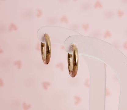 A pair of kids hypoallergenic rose gold hoop huggie earrings Displayed on clear acryllic stands with a soft pink background from the Pierced Peanut Earring Co in New Zealand, NZ.