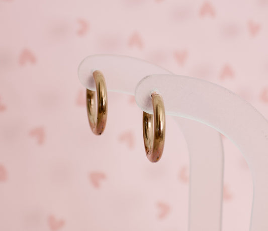 A pair of kids hypoallergenic rose gold hoop huggie earrings Displayed on clear acryllic stands with a soft pink background from the Pierced Peanut Earring Co in New Zealand, NZ.