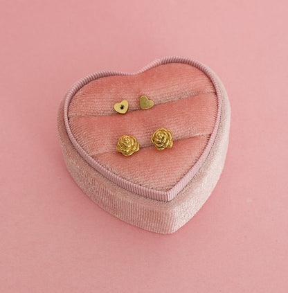 A pair of kids hypoallergenic gold earrings shaped like rose flowers, displayed on a pink heart shaped box. The earrings are screwback studs from the Pierced Peanut in Nz.