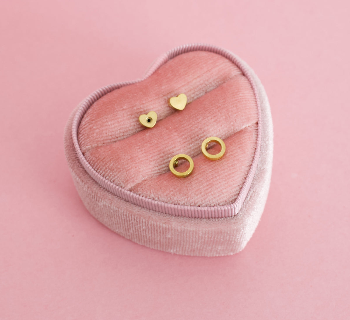 Two small gold open circle, halo ring stud earrings on a pink heart box. The earrings are for kids, made from hypoallergenic materials and are screwback studs from the Pierced Peanut Earring Co in New Zealand.