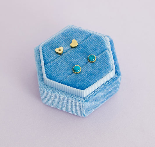 A pair of kids hypoallergenic blue marble and gold screwback stud earrings from The Pierced Peanut in Nz. Displayed on a blue ring box with the heart shaped screwbacks displayed above.