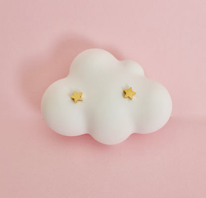A pair of kids small hypoallergenic gold star screwback stud earrings displayed on a white cloud-shaped jewellery stand against a soft pink background. Earrings are from the Pierced Peanut in New Zealand.