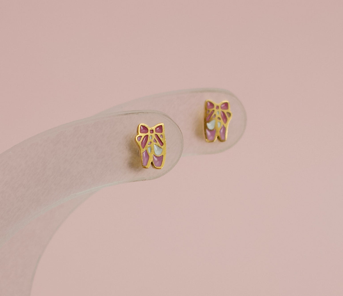A pair of kids hypoallergenic gold ballet shoe stud earrings displayed on a clear stand. The earrings are from the Pierced Peanut earring co in New Zealand.