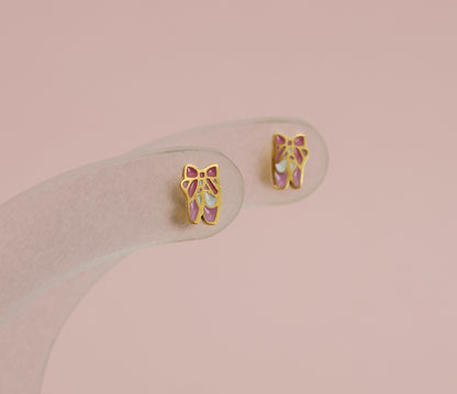 A pair of kids hypoallergenic gold ballet shoe stud earrings displayed on a clear stand. The earrings are from the Pierced Peanut earring co in New Zealand.