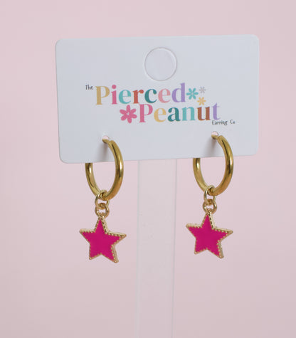 A pair of kids hypoallergenic gold huggies with pink star charms. Displayed on a white branded card from The Pierced Peanut Earring Co in New Zealand.