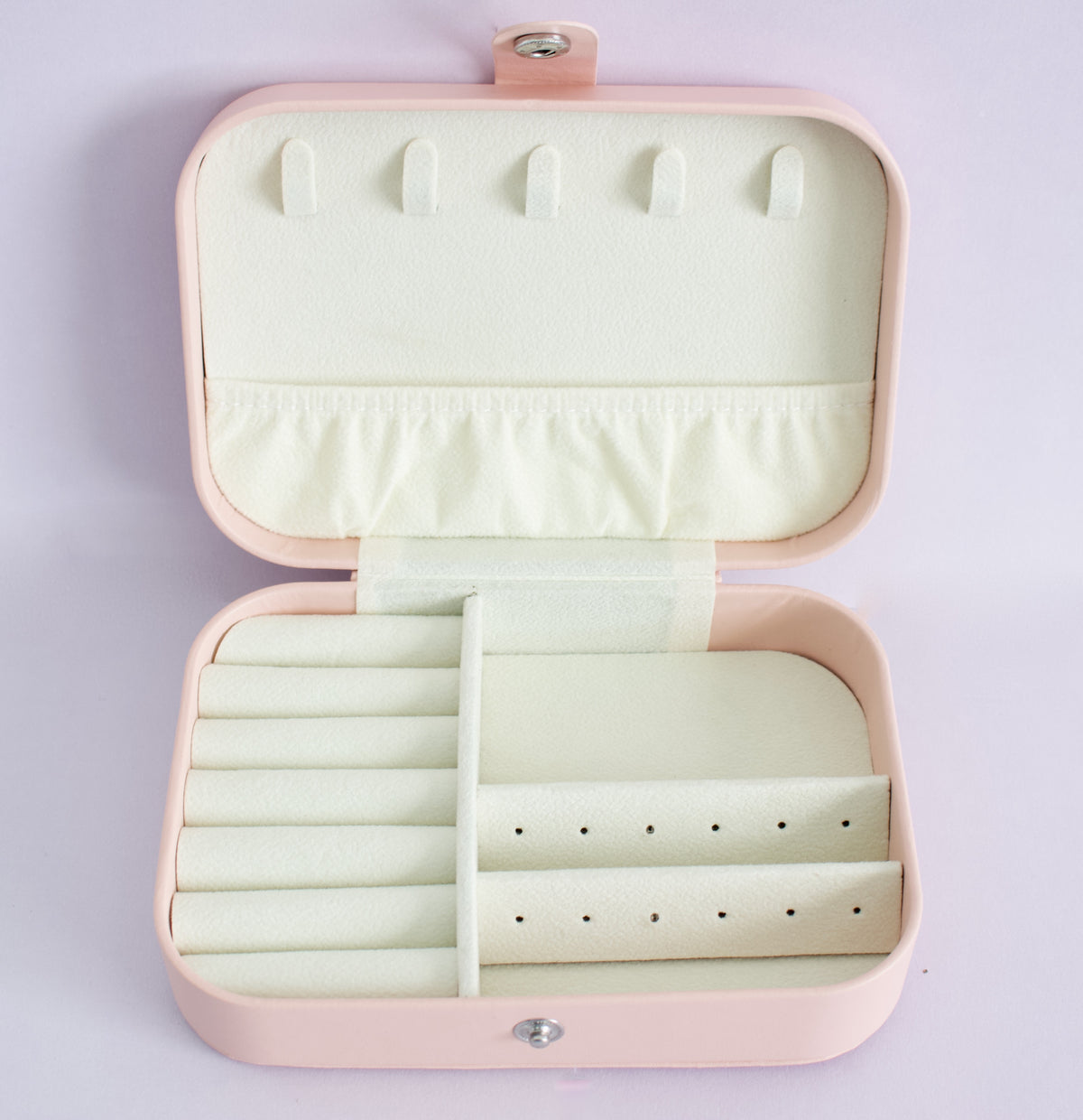 An open rectangular jewellery organiser case in pale pink, showing a cream-coloured interior with multiple compartments, ring rolls, and ear stud holes, photographed against a light lavender background from the Pierced Peanut Earring Co in New Zealand.