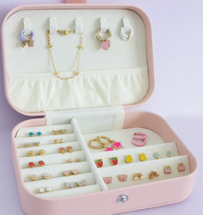 An open pink jewelry organizer box filled with earrings, rings, and a necklace, photographed on a pale lavender background from the Pierced Peanut in NZ.