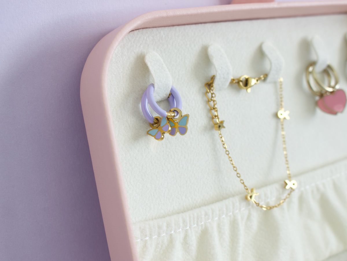Close-up of a pink jewellery organizer tray with white hooks holding pastel earrings and a gold star necklace on a light lavender background from the pierced peanut in nz.