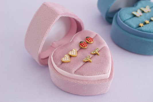 Gold heart-shaped stud earrings displayed in a pink velvet heart-shaped ring box, with a blue ring box partially visible in the background from the pierced peanut in nz.