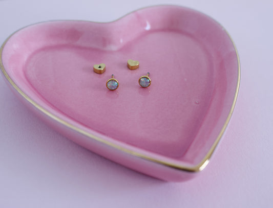 Two small gold stud earrings displayed inside a pink heart-shaped ceramic dish with a gold rim on a light pink background. Earrings are from the Pierced Peanut Earring Co in Nz.
